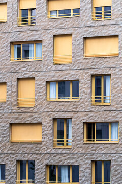 Modern apartment building facade in La Confluence, Lyon, France, with textured stone walls and warm yellow shutters creating a graphic residential pattern