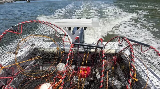 Commercial crab traps on moving motorboat on river with wake during sunny day.