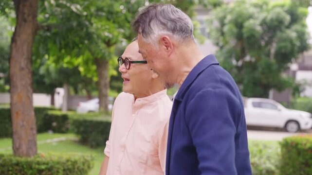 Happy Asian senior gay couple caring for each other during outdoor walk together in public park. Elderly retired people enjoy healthy aging, companionship family support and wellness healthy lifestyle