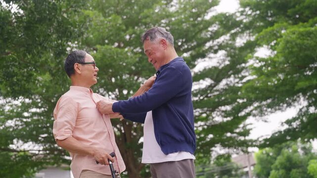Happy Asian senior gay couple caring for each other during outdoor walk together in public park. Elderly retired people enjoy healthy aging, companionship family support and wellness healthy lifestyle