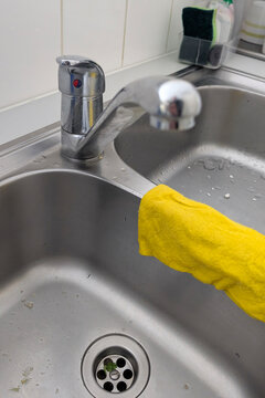 Cleaning a kitchen sink with a yellow cloth while water runs from the faucet