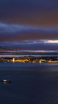 View of 25 de Abril Bridge famous tourist landmark of Lisbon connecting Lisboa and Almada over Tagus river in the evening twilight with tourist boats. Lisbon, Portugal. Camera pan