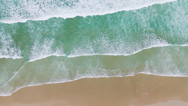 Aerial overhead view slow motion of ocean waves crashing onto sandy beach dynamic natural footage.