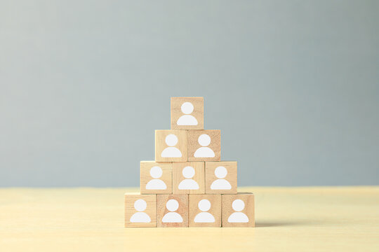 Wooden blocks with people icons arranged in a pyramid represent team hierarchy, organizational structure, leadership, workforce management, business network and human resources concept.