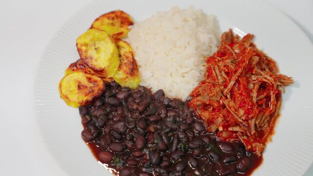 Pabellon criollo plate featuring white rice, black beans, shredded beef, and fried plantains. Traditional venezuelan cuisine.