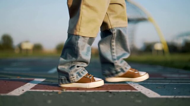 Placing brown sneaker on hopscotch square, child stepping across play court, showing denim pants