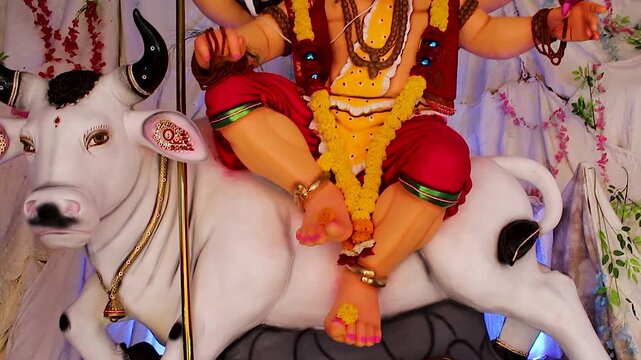Ganesh idol dressed as Lord Shiva holds trishul and damru with jib shot movement, marigold garlands decorate pandal during Ganesh Chaturthi festival India.