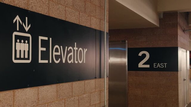 Static close-up of elevator and floor wayfinding signs beside closed elevator doors.