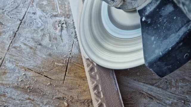 The process of cutting or grinding tiles with an angle grinder at a construction site. Close-up of a rotating diamond disc of a grinder, dust formation during construction and repair work.