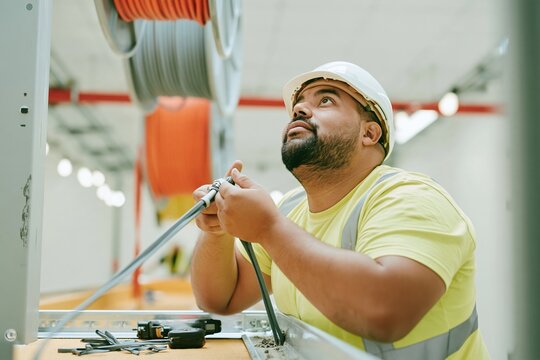 Floating cable drums hover over a man in a hard hat working in a dusty data center construction site, for infrastructure and technology marketing