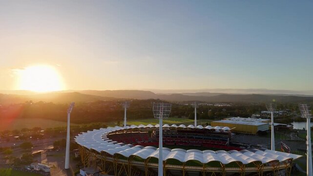 Cinematic aerial view of professional stadium during golden hour sunset over coastal mountains.