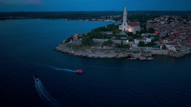 Aerial view of Rovinj, Croatia, at night, showing the illuminated historic old town, red-tiled rooftops, the Church of Saint Euphemia