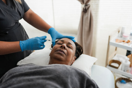 Senior african woman doing botulinum treatment inside private medical clinic - Beauty trends and anti aging concept - Focus on face