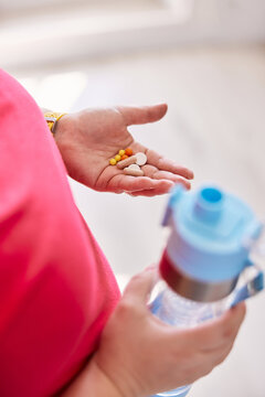 Person with water bottle and vitamins in hands