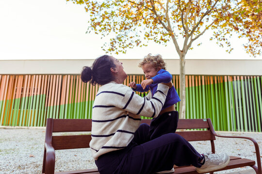 Mother holding and playing with happy child on a park bench, enjoying outdoor family moments