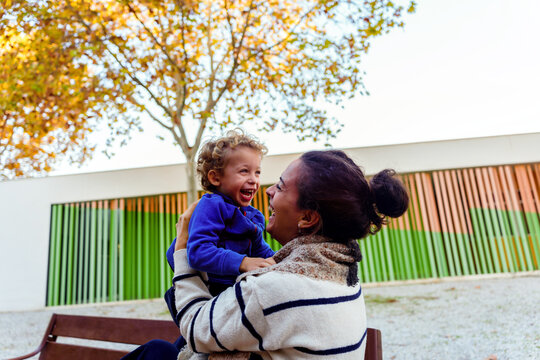 Mother and son sharing happy moment, woman holding child up, both laughing with joy in outdoor park setting