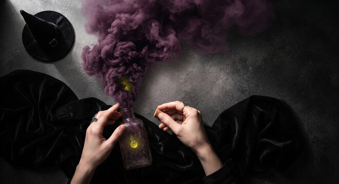 Witch hands holding a smoking magic potion bottle for halloween occult ritual