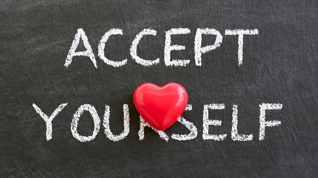 Accept yourself text written in white chalk on a dark slate blackboard background with a glossy red heart shape object placed centrally