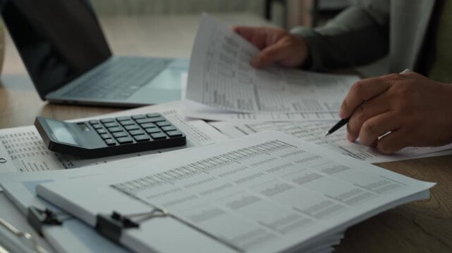 Close-up of businessman reviewing printed financial statements with pen beside calculator, analyzing expenses, revenue and costs for annual budget planning.