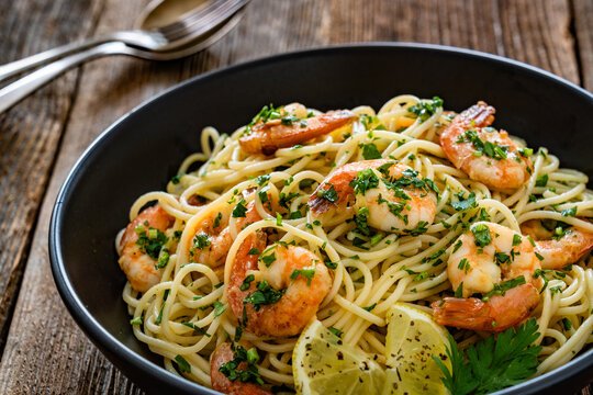 Spaghetti with fried shrimps, olive oil and parsley on wooden table