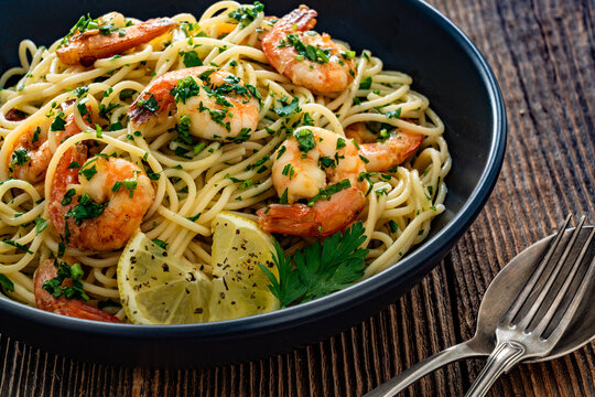Spaghetti with fried shrimps, olive oil and parsley on wooden table