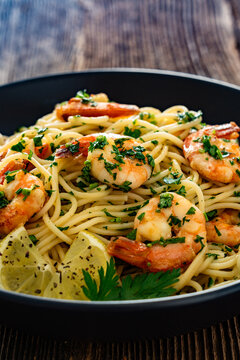 Spaghetti with fried shrimps, olive oil and parsley on wooden table