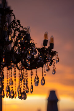 vintage crystal chandelier close up with sunset background vertical view, elegant crystal pendant chandelier reflecting golden twilight sky, ornate chandelier with candle bulbs against warm sunset hor
