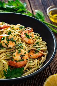 Spaghetti with fried shrimps, olive oil and parsley on wooden table