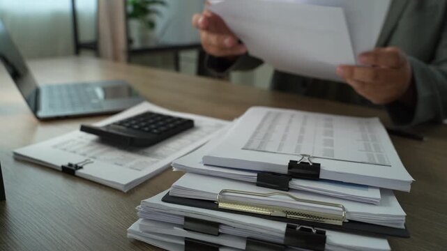 Businessman taking notes beside printed spreadsheets and laptop, showing accounting document review, financial reporting and office paperwork analysis.