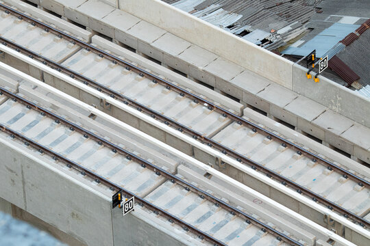 Concrete bridge supports railway tracks. Metal rails run parallel, aligned precisely. View from above highlights construction precision.