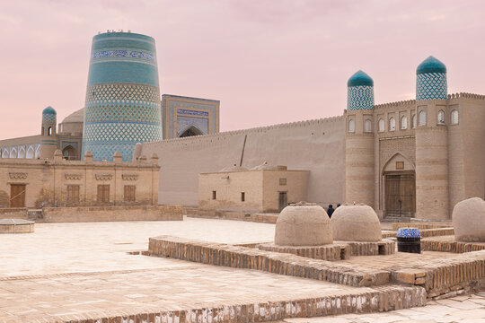 Kalta Minor minaret and fortress walls inside Ichan Kala at sunset in Khiva, Uzbekistan. Turquoise-tiled architecture against a pink twilight sky, ideal for travel and heritage publications.