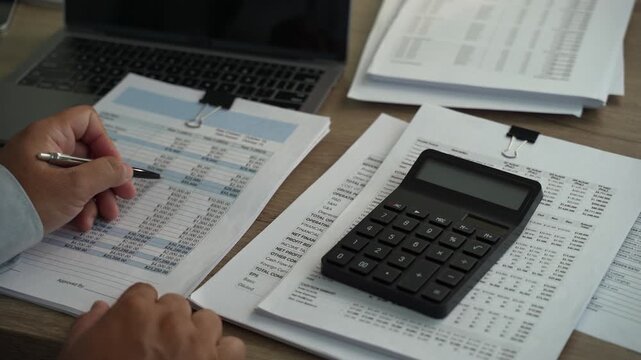 Hands using calculator on financial reports and tax documents, showing accounting audit analysis, financial calculation and business document review.