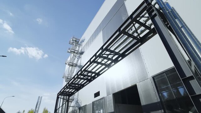 Large industrial building features sturdy metal external staircase. Robust metal fire escape extends along side of industrial facility