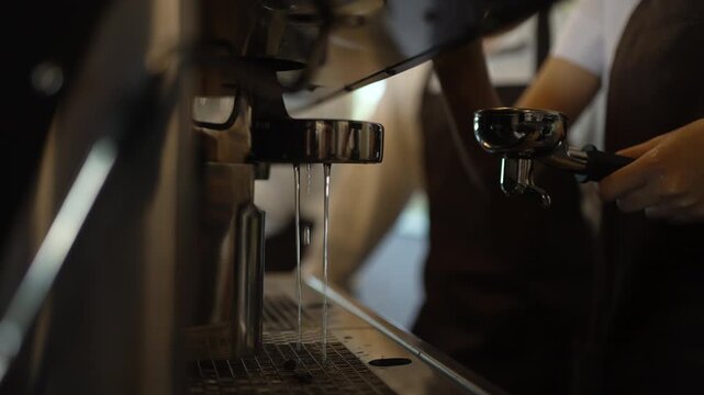 Barista trainee holds portafilter beside espresso machine water flow