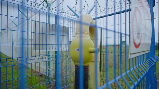 Gas metering station stands behind mesh fence topped with sharp barbed wire. Durable fencing and protective barbed wire surround equipment