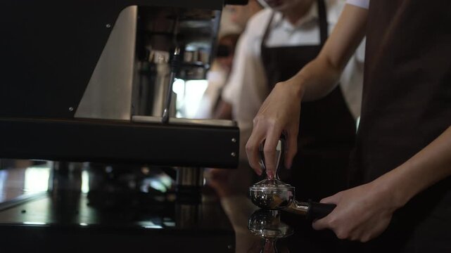 Barista trainee tamping coffee in a portafilter at an espresso machine