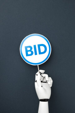 A white robotic hand holding a blue bidding paddle with "BID" signs on a dark gray background. Concept of artificial intelligence in auction and online bidding. Top view with flat lay.