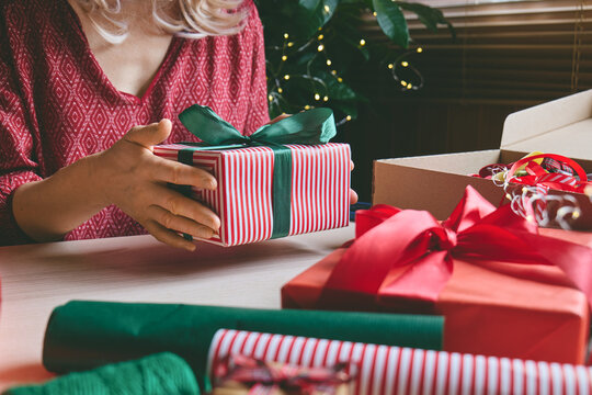 Woman carefully wrapping a gift with paper and ribbon at home.
The scene illustrates gift preparation, personalized shopping, product presentation and consumer gifting for special occasions.