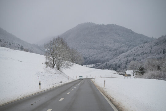 Mountain road and farmhouse at Orvin in winter, a car on the slippery winding road, Bern canton, Switzerland
