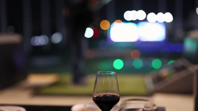A man practices golf at night with a glass of red wine in foreground bokeh lights add a dynamic and cinematic feel to the footage.