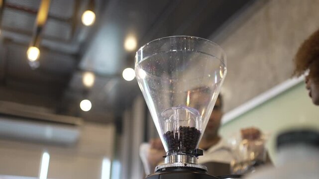 Barista trainee smiling behind coffee grinder hopper filled with beans