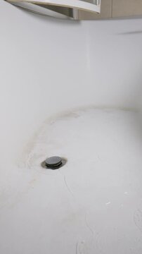 Water drains slowly around a metal stopper inside a stained white bathtub basin. The vertical composition offers clear copy space for home maintenance and hygiene concepts.