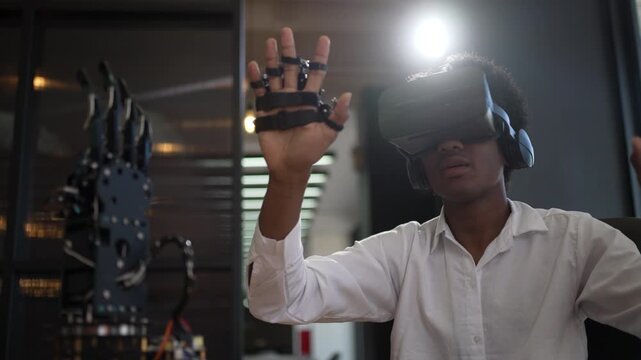Young man in VR headset raises both hands in a dim tech room