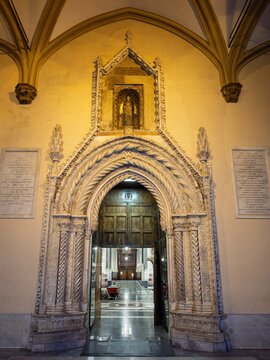 Symmetrical interior view looking through the ornate marble portal of Palermo Cathedral, revealing the illuminated nave and classical wooden doors framed by delicate stone carvings.