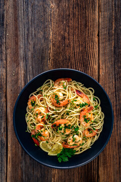 Spaghetti with fried shrimps, olive oil and parsley on wooden table. Top view