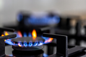 Gas burner with blue and orange flame. Close cooktop detail with softly blurred background.