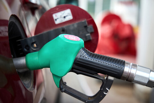 Green fuel pump nozzle with 95 unleaded gasoline label refilling red car tank at gas station close up view during auto service concept