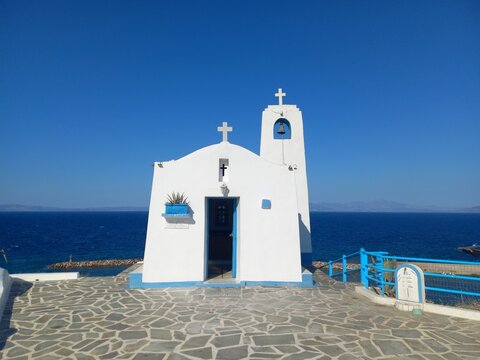 Tradizionale chiesa greco-ortodossa con mura bianche e dettagli blu su uno sfondo di cielo e mare blu intenso in Grecia.