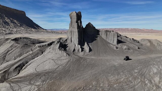 Drone Shot of All Terrain Vehicle Moving Under Grey Sandstone Rock Formations and Factory Butte, Utah USA