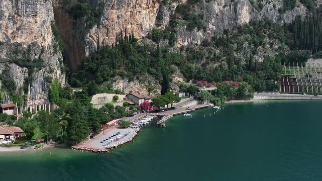 Cinematic 4k zoom drone shot of the quaint coastal village of Tignale in Northern Italy between the shores and sandy beaches of Lake Garda and dramatic cliffs that rise high above the town